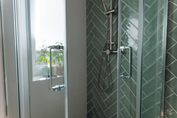Silver Glass door handle of a glass partition shower unit. Bathroom glass door detail with bath tub...