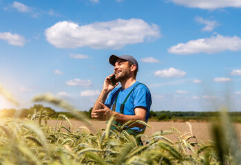 Candid photo of male agricultural worker talking on phone near grain field in countryside