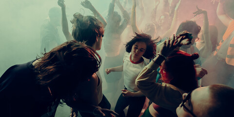 A lively crowd dancing with vibrant lighting and hazy atmosphere. Concept of party, concert, music, dance