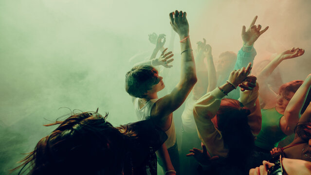 Young people dancing energetically at a vibrant music festival with colorful lighting and fog effects. Concept of concert, party, music, rhythm.