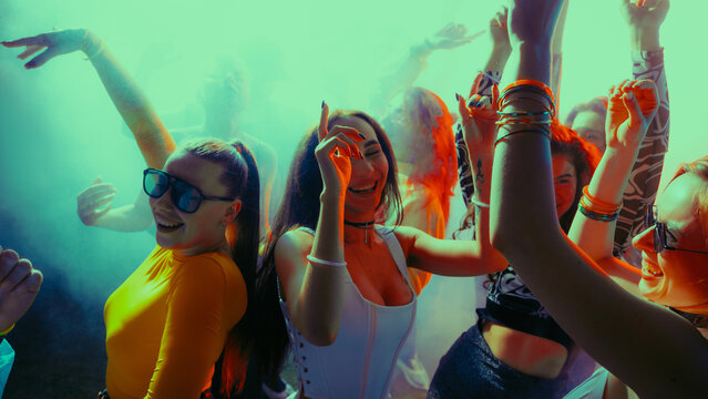 Crowd of young people dancing energetically in a vibrant party with colorful lights. Concept of nightlife, party, youth, summer, festivity, celebration