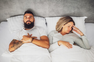 Couple is lying in bed. They are angry and not talking to each other.