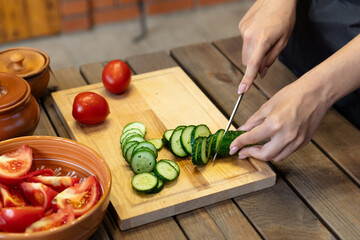 Person is slicing a cucumber on the wooden cutting board. The focus on fresh produce and the...