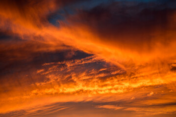 Dramatischer Wolkenhimmel, der von der unter- oder aufgehenden Sonne von unten orange angestrahlt...