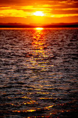 Unscharf gesteller Sonnenunter- oder Aufgang über dem Meer mit im Sonnenlicht glitzernden kleinen...