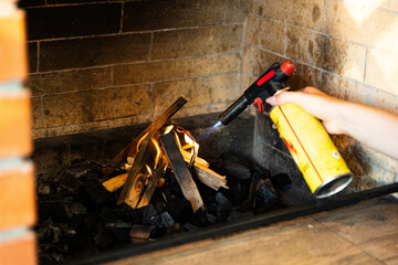 This image shows a fireplace being lit using a butane torch. The flame from the torch is helping...
