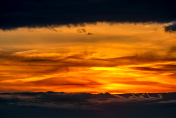 Die von Wolkenschleihern verdeckte, unter- oder aufgehende Sonne scheint durch ein sich in der...