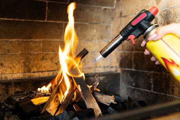 This image shows a fireplace being lit using a butane torch. The flame from the torch is helping...