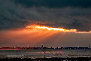 Aufbrechender, grauer Wolkenhimmel mit orange durchscheinendem Sonnenlicht über der Nordseeinsel...