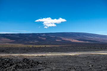 A single cloud drifts above the vast lava plains of Mauna Kea, captured from Saddle Road in the...