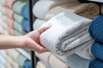 Customer hand choosing folded cotton bath towel from shelf at home decoration store. Soft textile stack collection for bathroom decor and hotel amenities