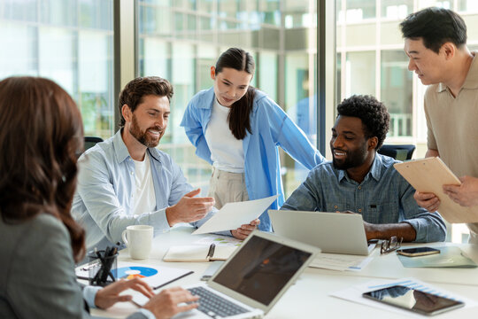 Diverse business team collaborating on project using laptop and documents in modern office