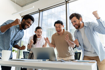 Excited business team celebrating success looking at laptop in office