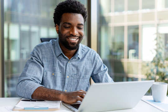 Smiling black businessman working on laptop in modern office