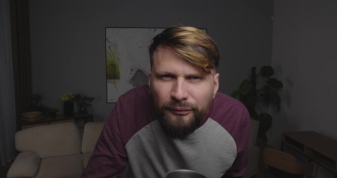 Close up funny European man with a beard looking to camera or  out window drinking from a cup and sees something there being shocked
