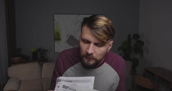 Close up bearded European manlookin to camera or  window holding sheets of paper in his hand. When he sees something frightening or shocking, he drops them