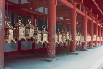 Golden bronze lanterns hanging between red columns at Kasuga Taisha Shrine in Nara Japan...