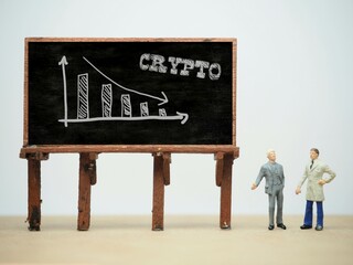 Mini toy of action figure at table with blurred background. Business financial photography concept design. Minifigure of businessman character with Crypto graph at blackboard. Down chart arrow.