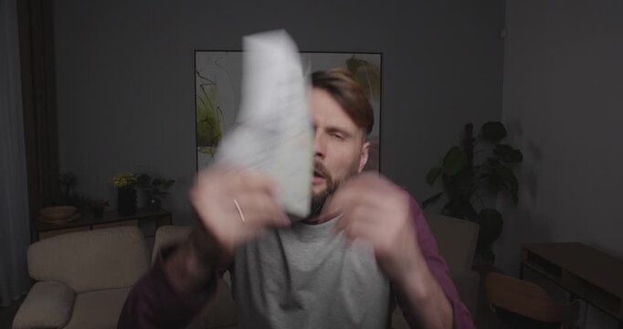 Close up bearded European manlookin to camera or  window holding sheets of paper in his hand. When he sees something frightening or shocking, he drops them