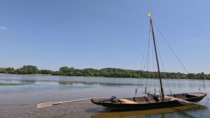 Traditional wooden sailing scow floats moored in shallow river current
