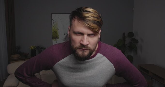 Close-up of a funny, bearded guy looking into the camera, a mirror, or a window, bracing himself for an important meeting. He takes a deep breath and strikes a superhero pose.