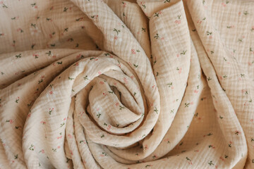 Close-up of soft beige muslin fabric with tiny floral print, artistically rolled into a spiral....