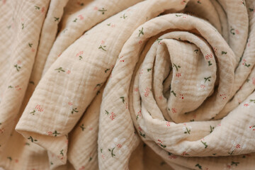 Close-up of soft beige muslin fabric with tiny floral print, artistically rolled into a spiral....