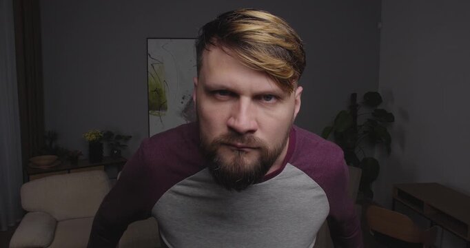 Close-up of a funny, bearded guy looking into the camera, a mirror, or a window, making funny agressive face