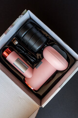 Pink massage gun with black attachments and USB cable in original box on dark background. Portable...