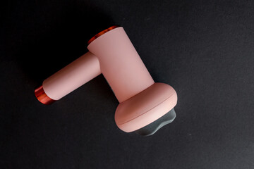 Close-up of pink handheld massage gun on black background. Modern portable device for muscle...
