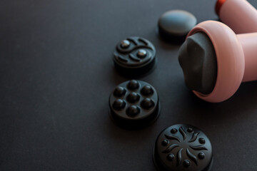 Pink massage gun with soft head and four different black attachments arranged on dark background....