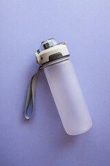 Minimalist sports water bottle with carrying strap and flip-top lid on a light purple background....