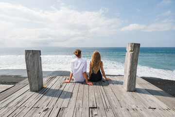 Romantic Couple Sitting on Wooden Deck by Ocean.