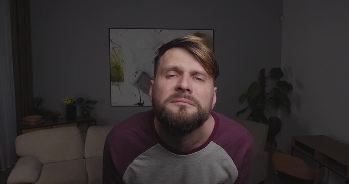 Close-up of a bearded blond man crying funny, stretching out his hands to the camera, standing in a room at home.
