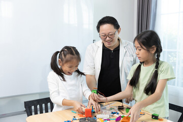 Smiling teacher guides two girls building colorful STEM robotics projects, fostering creativity, problem-solving, and teamwork through engaging hands-on learning activities.