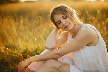 Beautiful woman relaxing in a golden meadow at sunset