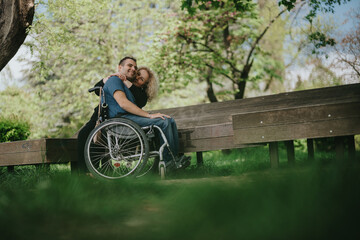 A touching moment of companionship and affection, featuring a man in a wheelchair and a woman sharing a hug while sitting beside a wooden bench among lush greenery and vibrant trees.