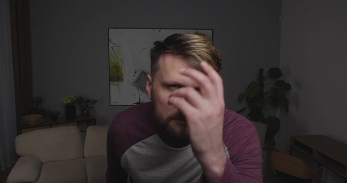 Close-up of a funny, bearded guy looking into the camera, a mirror, or a window, making funny agressive face and fixing his hair with hand