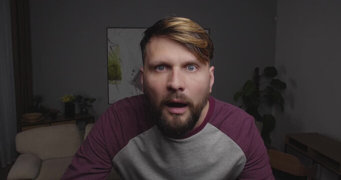 Close-up of a funny, bearded guy looks at the camera or out the window in surprise, his jaw dropped and his mouth open