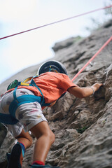 Low angle view of child rock climbing with helmet and harness on natural wall