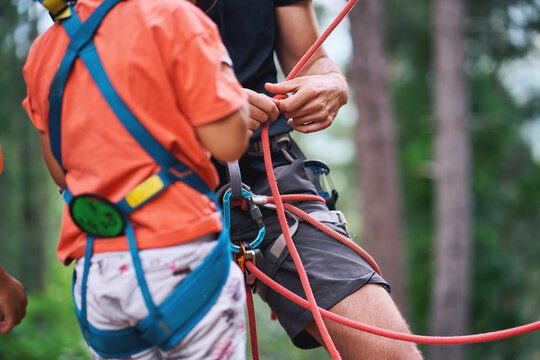 Instructor adjusting climbing rope on child’s harness in outdoor training - Powered by Adobe