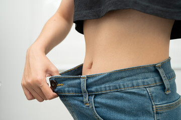 Young Asian woman losing weight wearing loose pants in oversize jeans.