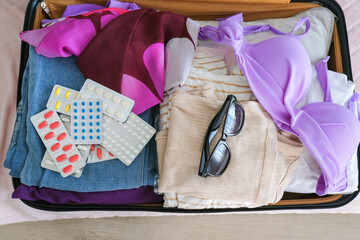 Women's clothing and pills in a travel bag. Concept of medication required in journey. Top view
