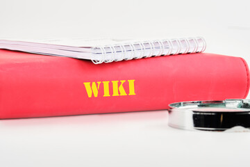A red binder titled Wiki is placed alongside a spiral notebook and a magnifying glass, symbolizing...