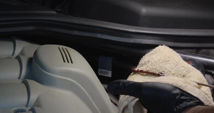  Male hands in gloves check the oil level with a dipstick in a car. Taking care of the engine compartment