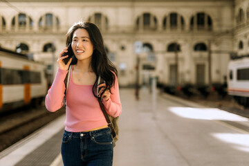 Chinese woman smiling and talking on the phone at a train station during a sunny day