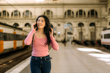 Chinese woman on phone at a bustling train station with trains arriving in the background