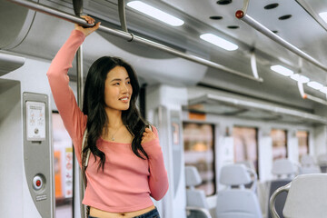 Chinese woman enjoying a journey on a train while standing and holding onto the overhead bar in a...