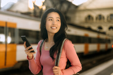 Chinese woman waiting at a train station with a phone in hand and a smile on her face