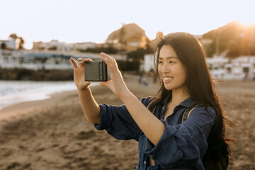 Chinese woman enjoying sunset at the beach while taking pictures